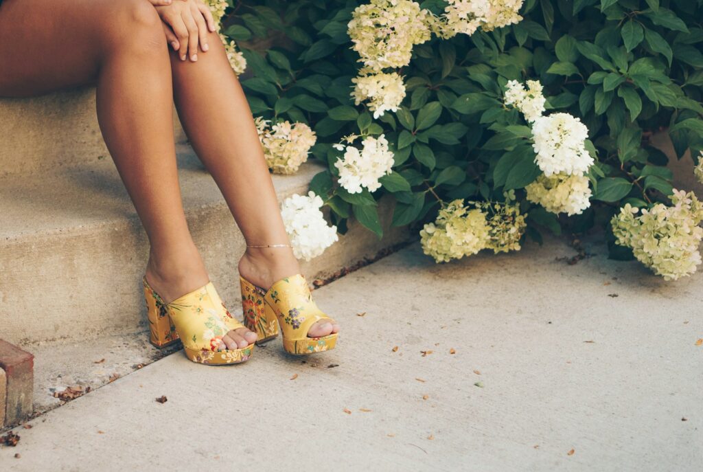 woman sitting on brown stair beside yellow and white flowers