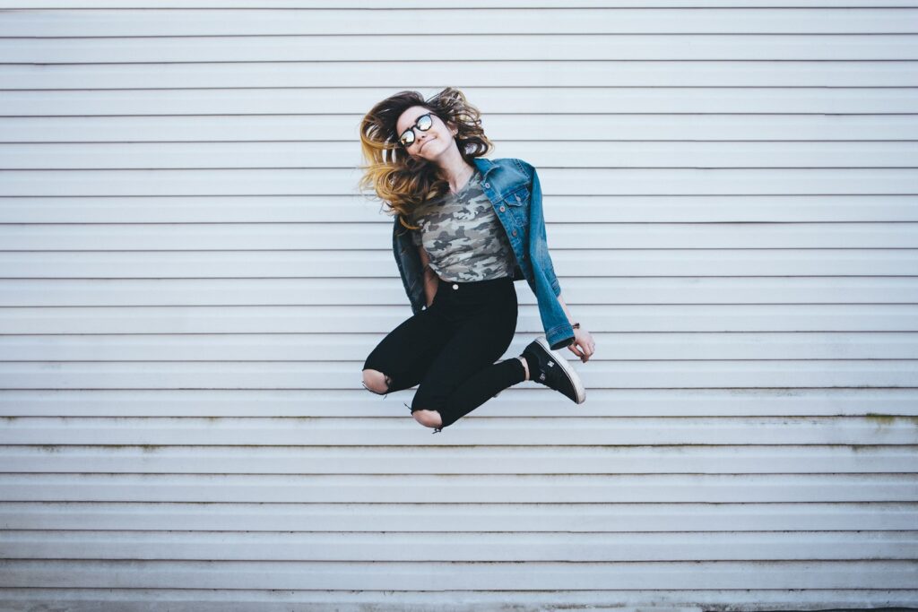 woman jumping in front of white concrete establishment